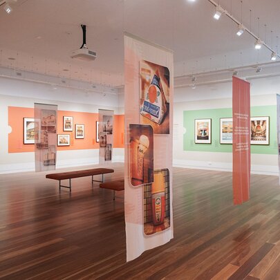 A gallery hung with artwork with a polished wooden floor and green and orange feature walls