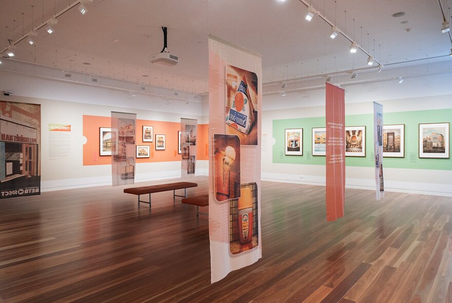 A gallery hung with artwork with a polished wooden floor and green and orange feature walls