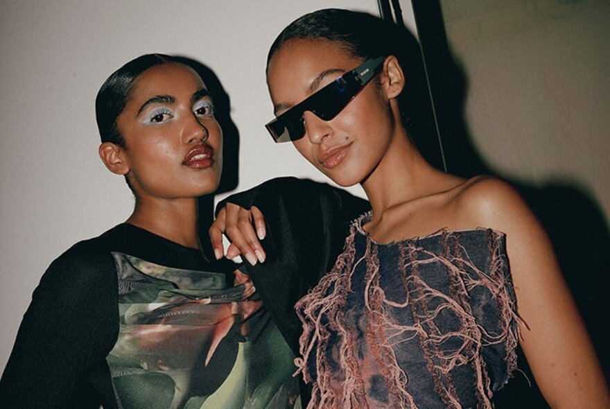 Two fashion models, one wearing 1990s style sunglasses, posed and looking at the camera.