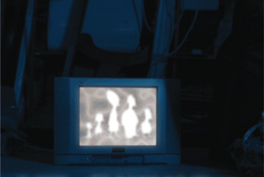 A vintage television set placed in a dark environment, displaying a glowing abstract light silhouette image of several rounded, organic figures on screen.