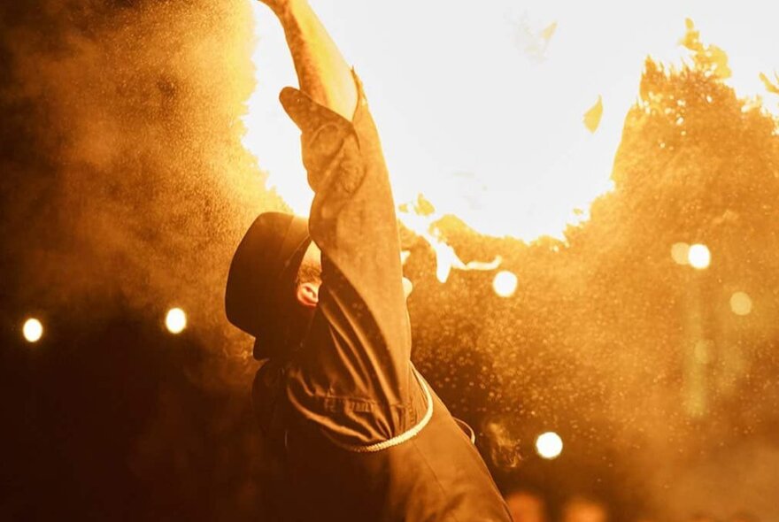 A fire-breathing performer, seen from behind, against shadowy night sky, as part of the Firelight Festival.