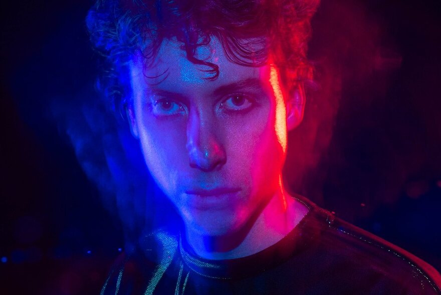 Blue and purple lit fractured portrait of a young man against a dark background.