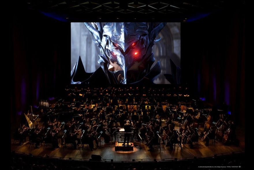 A dark image of the Melbourne Symphony Orchestra performing while a large screen displays a film on the background. 