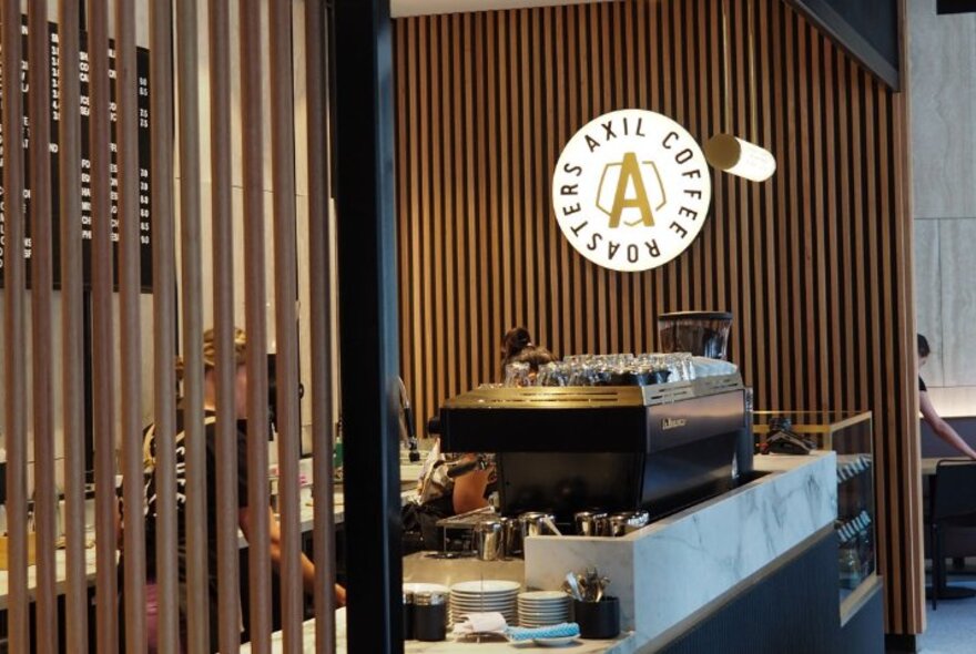 The coffee service counter of Axil Coffee at Flinders Gate, with a logo on the wall and a large coffee machine.