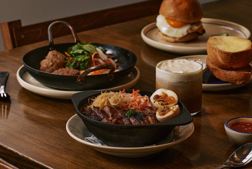 A selection of Vietnamese dishes displayed in black hot pots and skillets, on a wooden table.