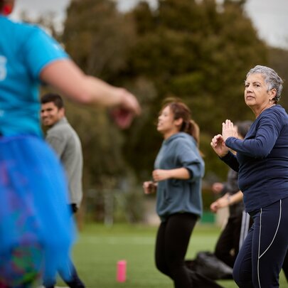 An outdoor group fitness class in a park with several participants of different ages exercising on the grass.