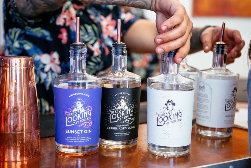 A hand turning some bottles of spirits, with different coloured labels, on the counter top of a bar.