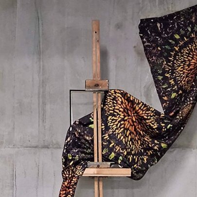 A printed swatch of fabric hanging from a solid concrete wall and draped over a wooden easel.