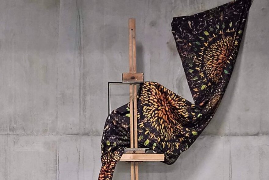 A printed swatch of fabric hanging from a solid concrete wall and draped over a wooden easel.