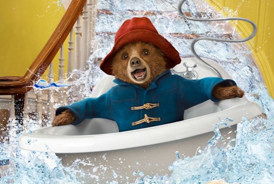 A still from the movie, Paddington, showing a bear in a blue duffel coat and a red hat floating down the stairs in a bathtub.