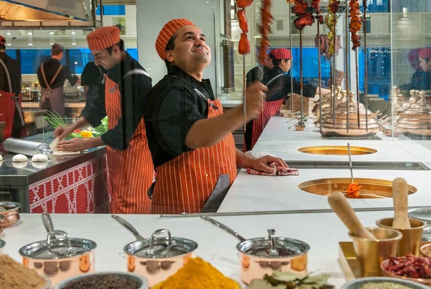 Chefs in orange aprons working at food stations with copper pans.