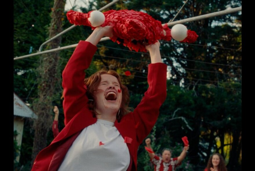 A woman screaming and holding a red and white object above her head beneath a clothesline.