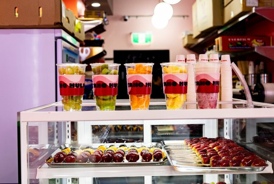 Dessert takeaway counter with rows of fruit on sticks and plastic cups of fruit.