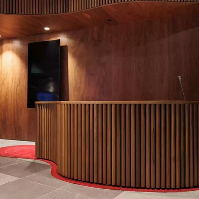 A curved reception desk at Koorie Heritage Trust features vertical wood slat panelling, with a timber wall behind and soft lighting.