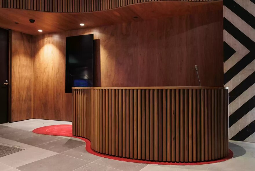 A curved reception desk at Koorie Heritage Trust features vertical wood slat panelling, with a timber wall behind and soft lighting.