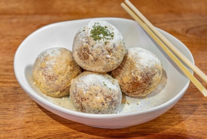 A bowl of large cheese balls with a set of chopsticks balancing on the bowl.  