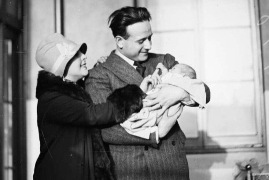 A couple holding a baby, wearing clothes from the 1940s, black and white image.