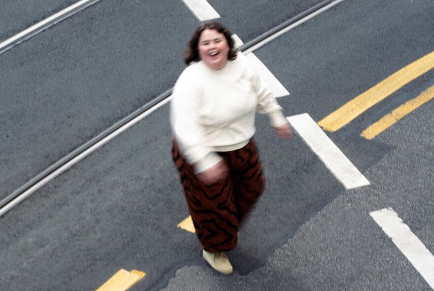 Looking down from above at comedian Taylor Griffiths walking across a road with white and yellow markings. 