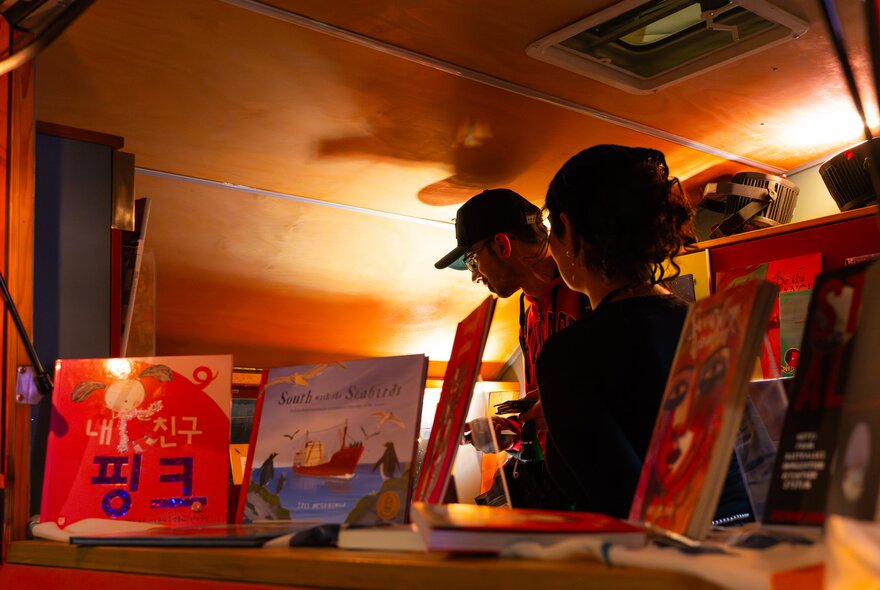 Two people inside a low-lit caravan that has multilingual books on display.
