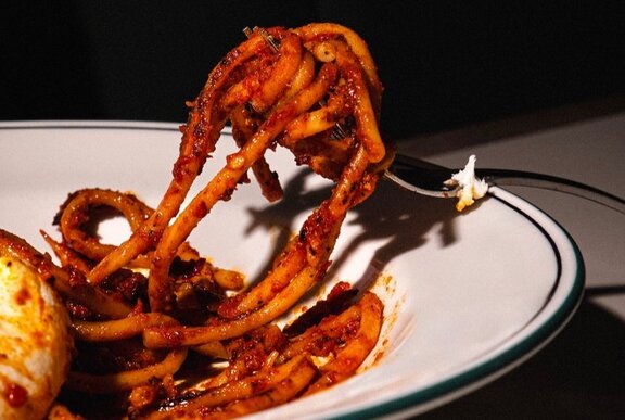 A fork twirling red spaghetti from a white bowl.