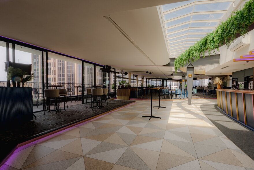 An empty bar space with a triangular patterned floor and indoor greenery. 