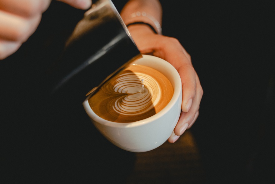 A hand pouring milk from a jug into a cup to create latte art. 