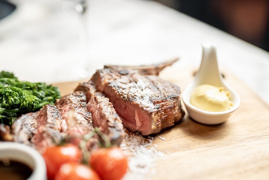 Sliced steak on a board with sauce and tomatoes.