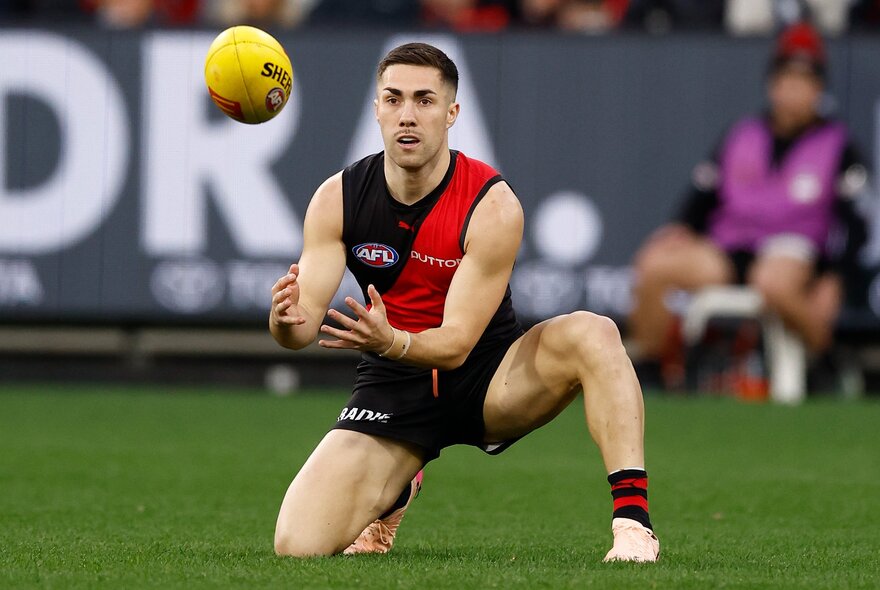 An Essendon AFL football player on the field during a match marking a ball.