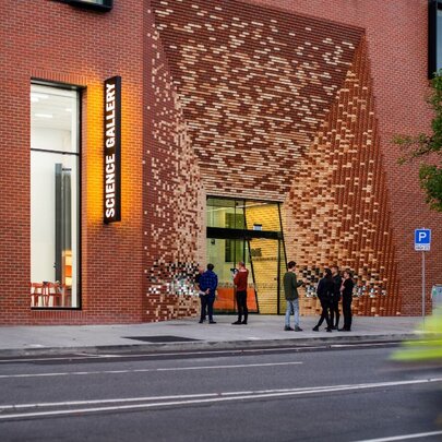 A tall brick building with people outside and a large detailed entrance. 