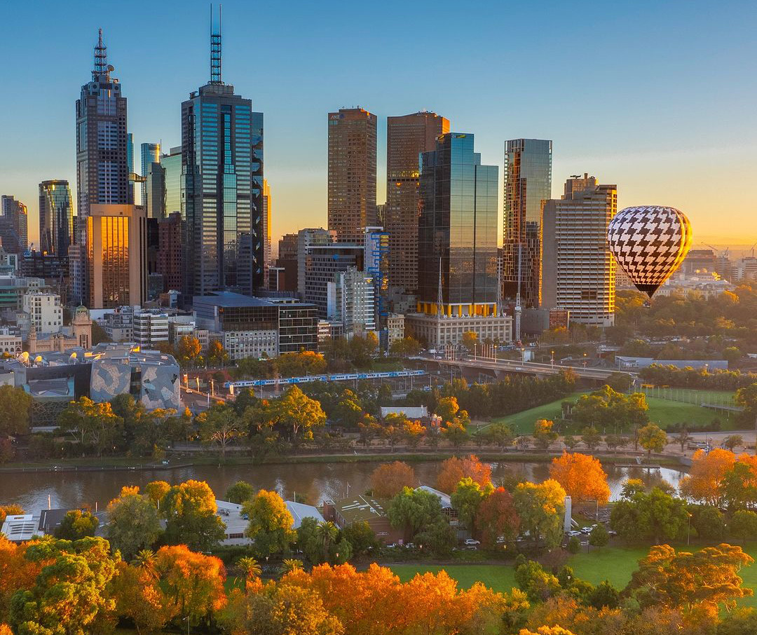 A black and white hot air balloon flying over an autumnal city scene.