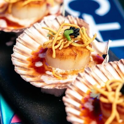 Close up of three seared scallops in their shells with a garnish of dry fried noodles.
