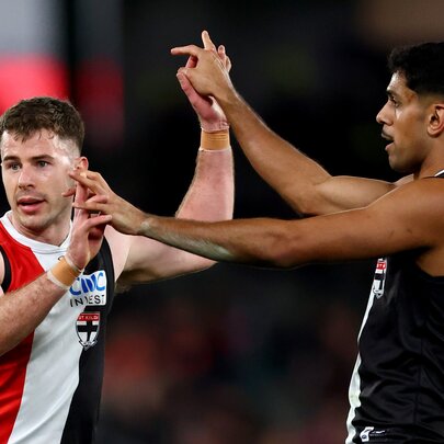 Two AFL players in St Kilda jerseys giving each other a double high five during a game.