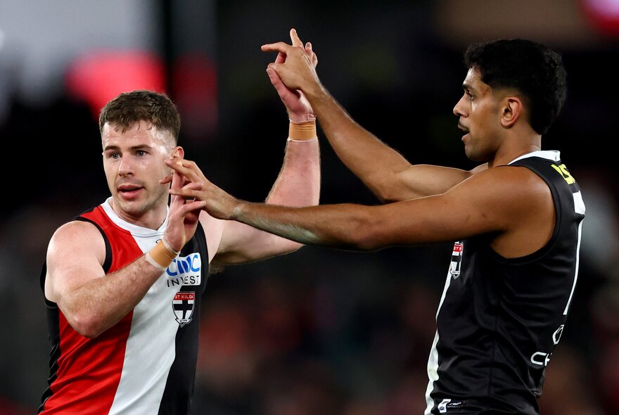 Two AFL players in St Kilda jerseys giving each other a double high five during a game.