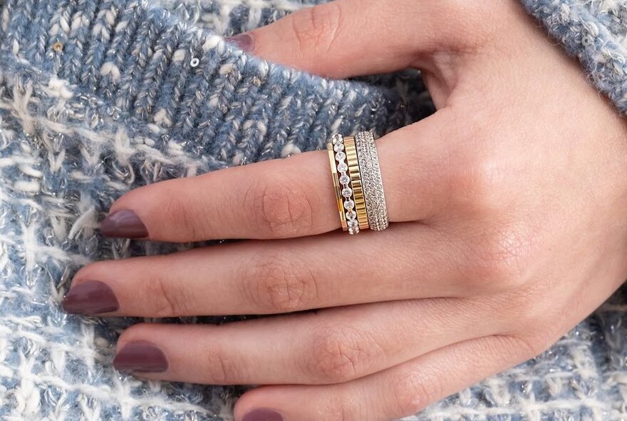 A woman's hand with several rings on her index finger, lightly resting on a woollen garment.