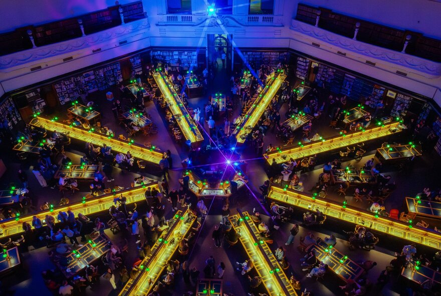 The Dome reading room of State Library Victoria at night, showing rows of desk fanning out from the centre lit up with yellow light.