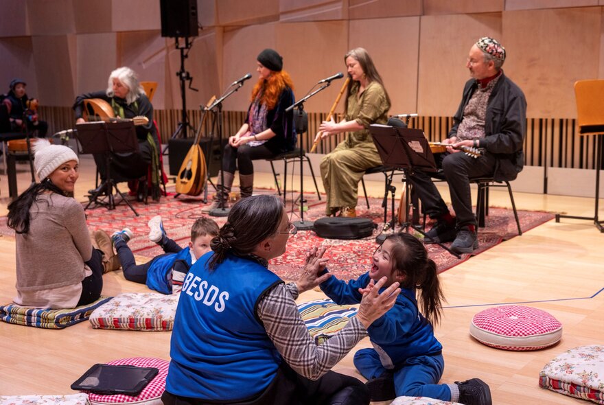A relaxed performance at the Melbourne Recital Centre, with seated musicians playing to an audience of young children and their carers sitting on the floor in a relaxed manner. 