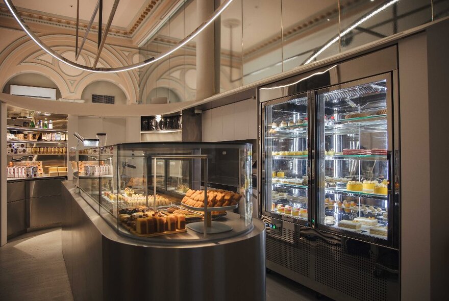 The high-ceiling and stylish interior of Le Yeahllow with cakes and desserts on display in refrigerated glass cabinets.