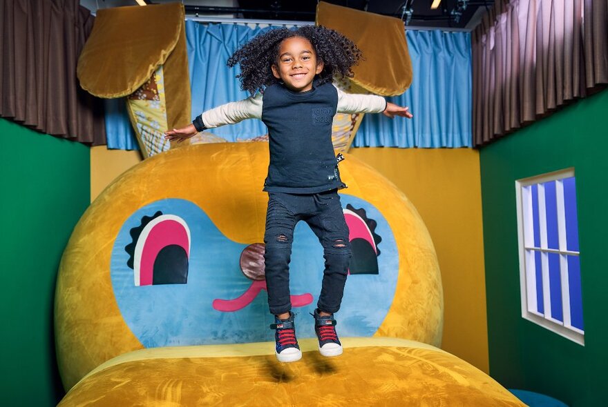 A young child jumping on a large plush bunny rabbit inside a small room with a window.