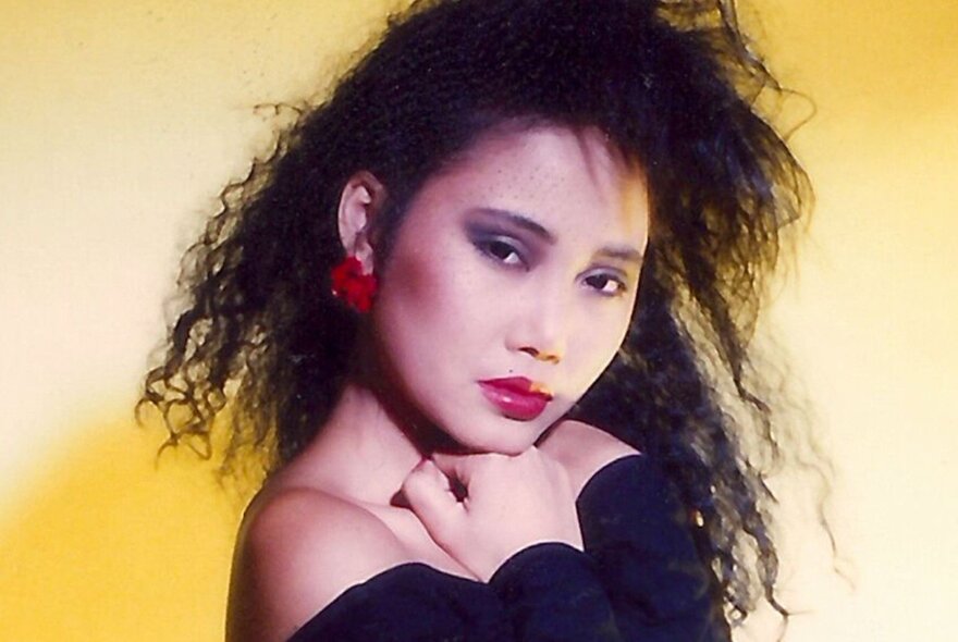 A woman frizzy hair and large red earrings with her hands up to her face looking serious. 