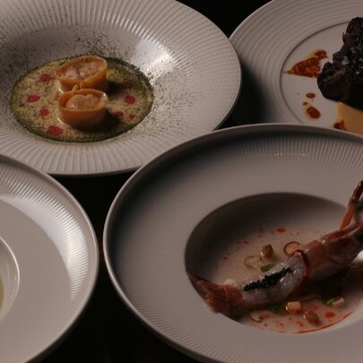 Four plates of food, including one with a full lobster, clustered together on a table.