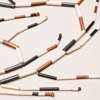 Short, cylindrical beads or components in white, copper, and blackened metal finishes, as part of a contemporary jewellery piece. 