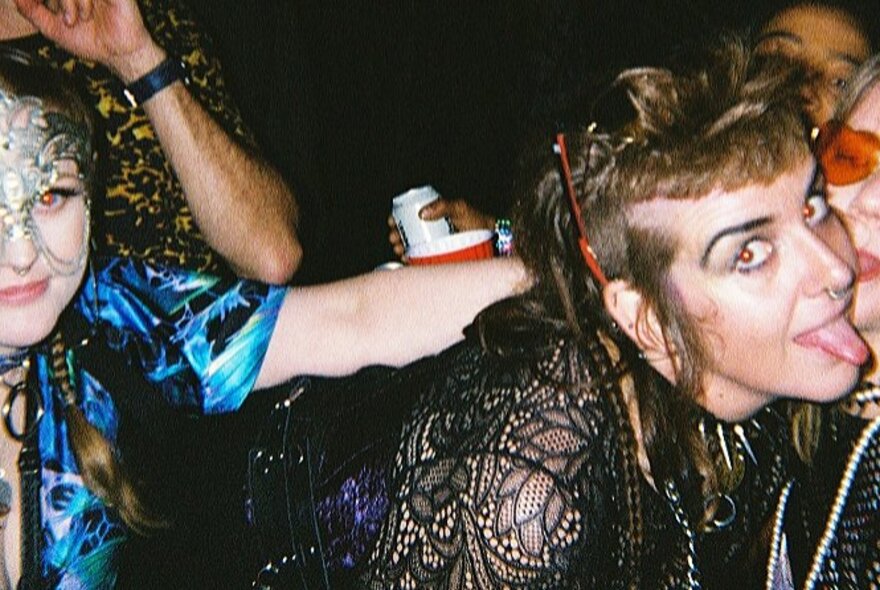 Revellers dancing at a wild party, one person looking at the camera with their tongue poking out.