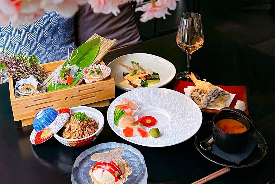 A dining table with several plates of food on it, a wine glass and small bowls.