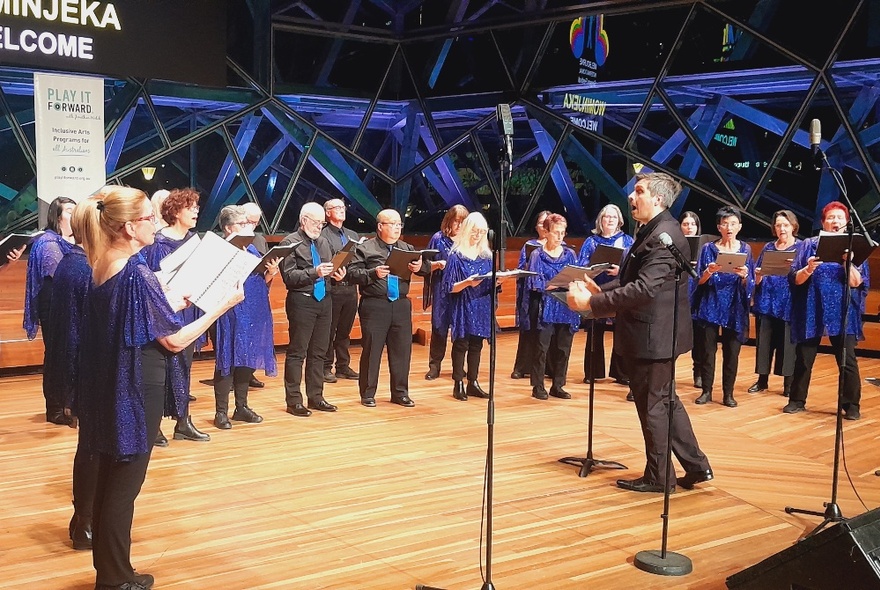 Conductor leading a choir performing on a wooden stage.