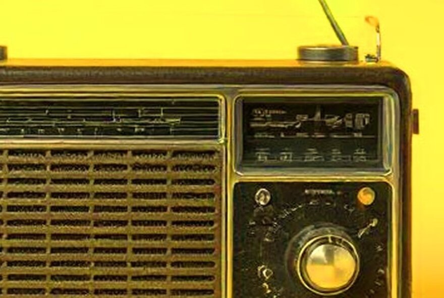 A close up of an old fashioned transistor radio, against a yellow background.
