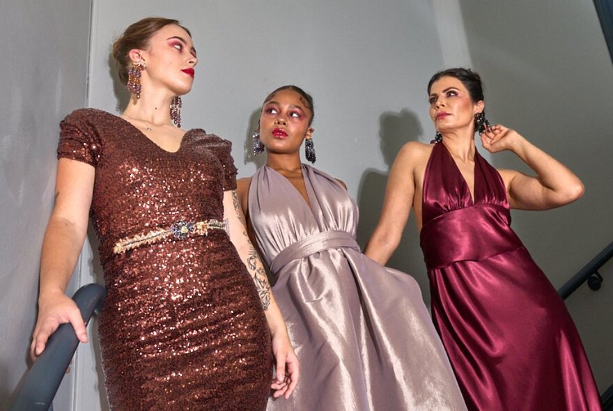 Models wearing shimmering evening gowns on a staircase.