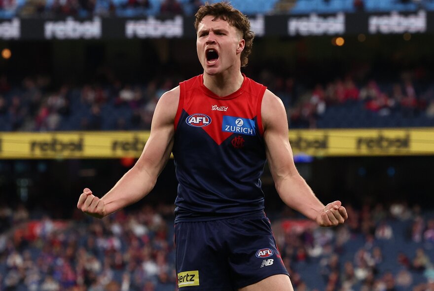 A Melbourne football player clenching his fists and yelling during a match. 