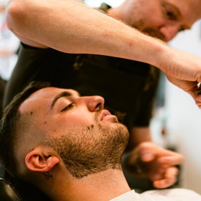 A barber holds a blade over a client in a chair receiving a neck shave. 