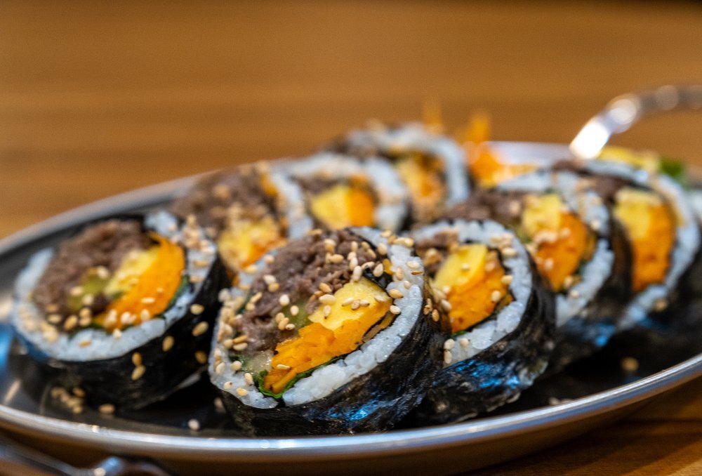A silver tray of sliced gimbap wrapped in seaweed, filled with beef and sprinkled with sesame seeds.