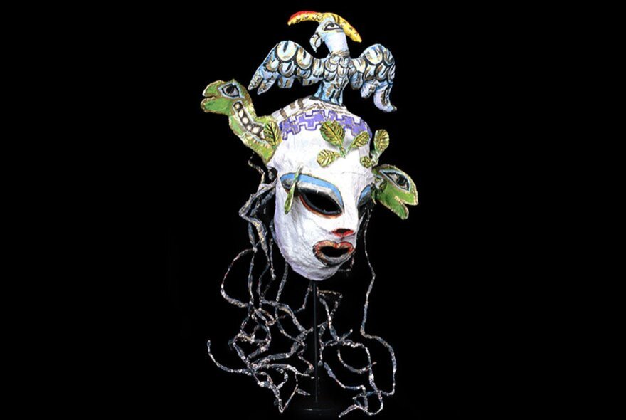 A plaster masquerade mask with turtle heads and a mystical bird coming out of the top, and long silver threads hanging down like hair.